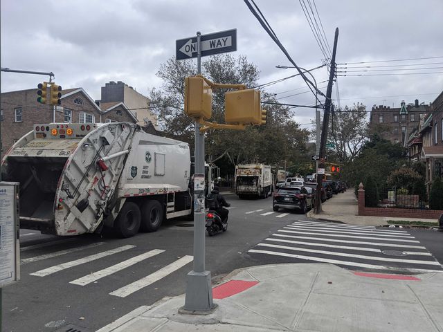 Two white garbage trucks drive down a city street.
